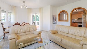A living room with two beige leather sofas, a glass coffee table, and a dining area with wooden chairs and a table. - Holiday Home 'Limonita' with Private Pool, Wi-Fi and Air Conditioning (Mutxamel)