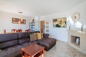 Uma sala de estar com sofá modular, uma mesa de centro de madeira, lareira e um espaço de jantar com cadeiras e mesa.