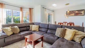 A modern living room with a sectional sofa, a wooden coffee table, and a dining area with wooden chairs. - Villa 'Los Naranjos' with Private Pool, Wi-Fi and Air Conditioning (Mutxamel)