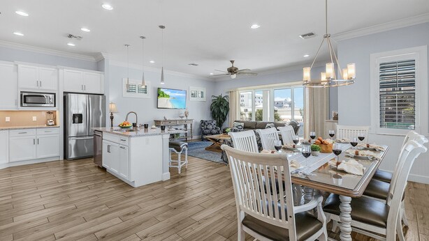 A spacious kitchen with white cabinets, a central island, and a dining area with a wooden table and white chairs. - Ocean view, Tiki, Heated Pool, Game Room - The Seahorse - Roelens (Fort Myers Beach)