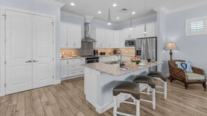 A modern kitchen with white cabinets, a central island with stools, stainless steel appliances, and pendant lighting. - Ocean view, Tiki, Heated Pool, Game Room - The Seahorse - Roelens (Fort Myers Beach)