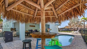 An outdoor pool area with a thatched roof, a bar, and a poolside seating area. - Ocean view, Tiki, Heated Pool, Game Room - The Seahorse - Roelens (Fort Myers Beach)