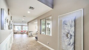 A spacious hallway with a tiled floor, a large abstract painting on the wall, and a view into a living area with a sofa and a table. - Copper View-Modern 4BR, Casita, Green Valley (Henderson)