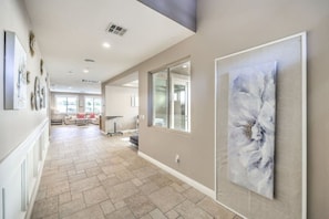 Un hall spacieux doté d’un sol carrelé, d’un grand tableau abstrait accroché au mur et donnant sur un espace de vie comprenant un canapé et une table.