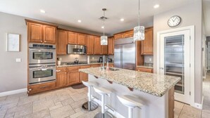 A modern kitchen with granite countertops, stainless steel appliances, wooden cabinets, and a large island with bar stools. - Copper View-Modern 4BR, Casita, Green Valley (Henderson)
