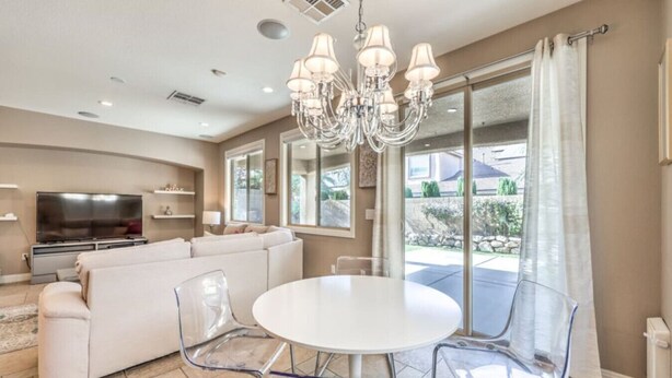 A modern living room with a white sofa, a TV, a chandelier, and a dining table with clear chairs. - Copper View-Modern 4BR, Casita, Green Valley (Henderson)