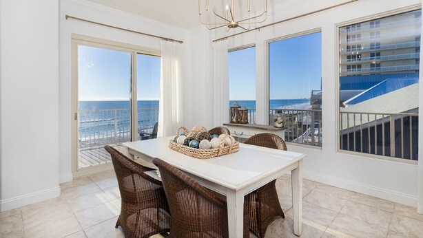 A dining area with a white table and wicker chairs, large windows with ocean views, and a chandelier. - Treasure Island 312 | Elite 3BR View (Panama City)
