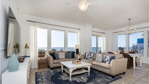 A spacious living room with a large window, a ceiling fan, and a view of the ocean. - Treasure Island 312 | Elite 3BR View (Panama City)