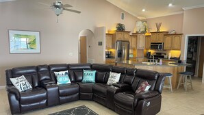 A modern living room with a sectional sofa, a ceiling fan, and a kitchen area with wooden cabinets and stainless steel appliances. - Three Bedroom Lakefront in home in Quaint Lake Placid Florida (Lake Placid)