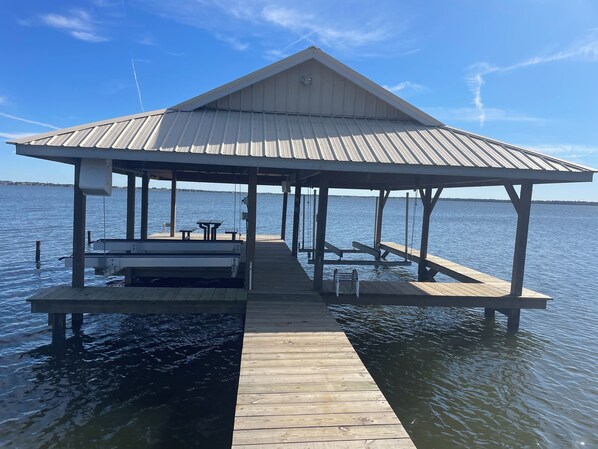 A wooden dock with a covered pavilion, benches, and tables.