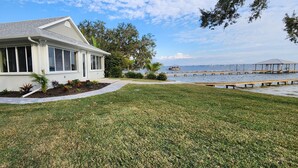 A house with a well-maintained lawn, a dock extending into a body of water, and a gazebo in the distance. - Three Bedroom Lakefront in home in Quaint Lake Placid Florida (Lake Placid)
