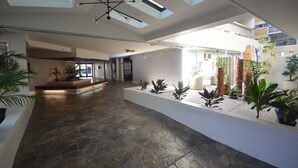 A spacious indoor area with a stone floor, a patterned wall, and several potted plants.