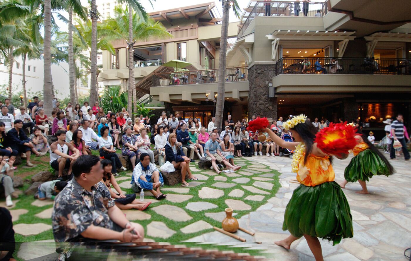 A hotel lobby with a stone floor, palm trees, and a crowd of people watching a performer.