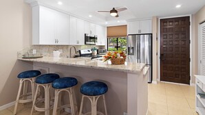 A modern kitchen with white cabinets, a stainless steel refrigerator, and a bar stool area. - 🏖️Ocean View Kona Condo w/ AC | Golf Course + Lanai (Kailua Kona)
