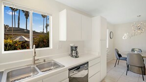 Een moderne keuken met witte kasten, een inbouwvaatwasser en een raam met uitzicht op palmbomen.