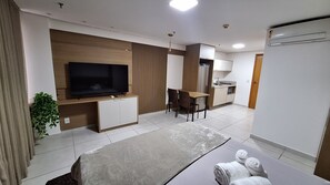Une chambre d’hôtel moderne équipée d’une télévision à écran plat, d’un coin repas, d’une kitchenette et d’un lit avec des serviettes.