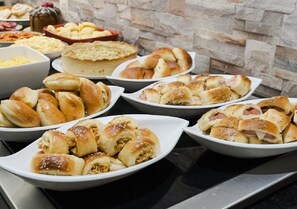 Un buffet proposant une variété de produits de boulangerie, notamment des petits pains, des viennoiseries et un gâteau.
