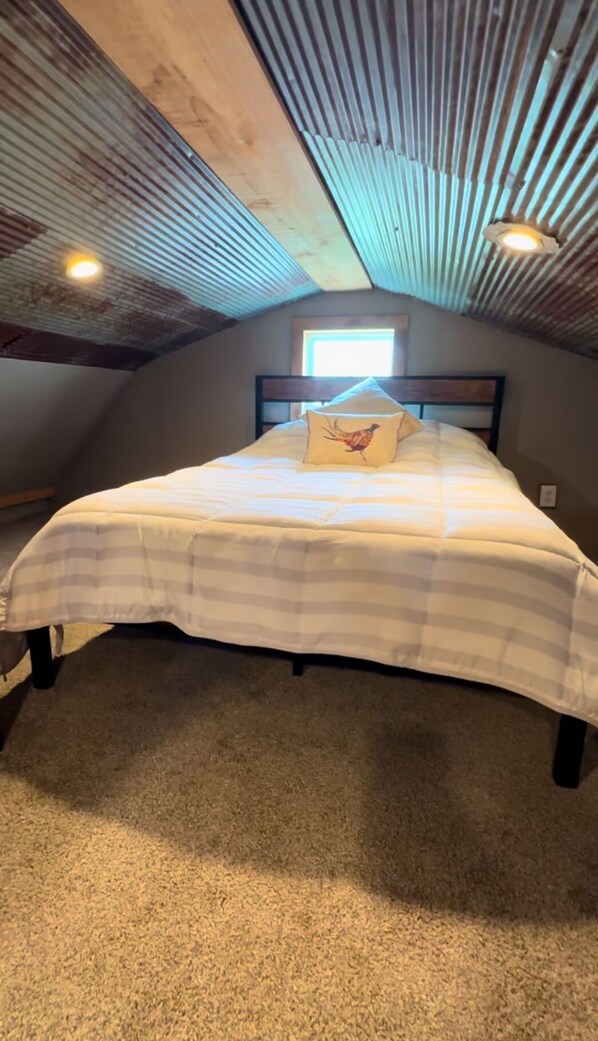 A bedroom with a bed, a window, and a sloped ceiling.