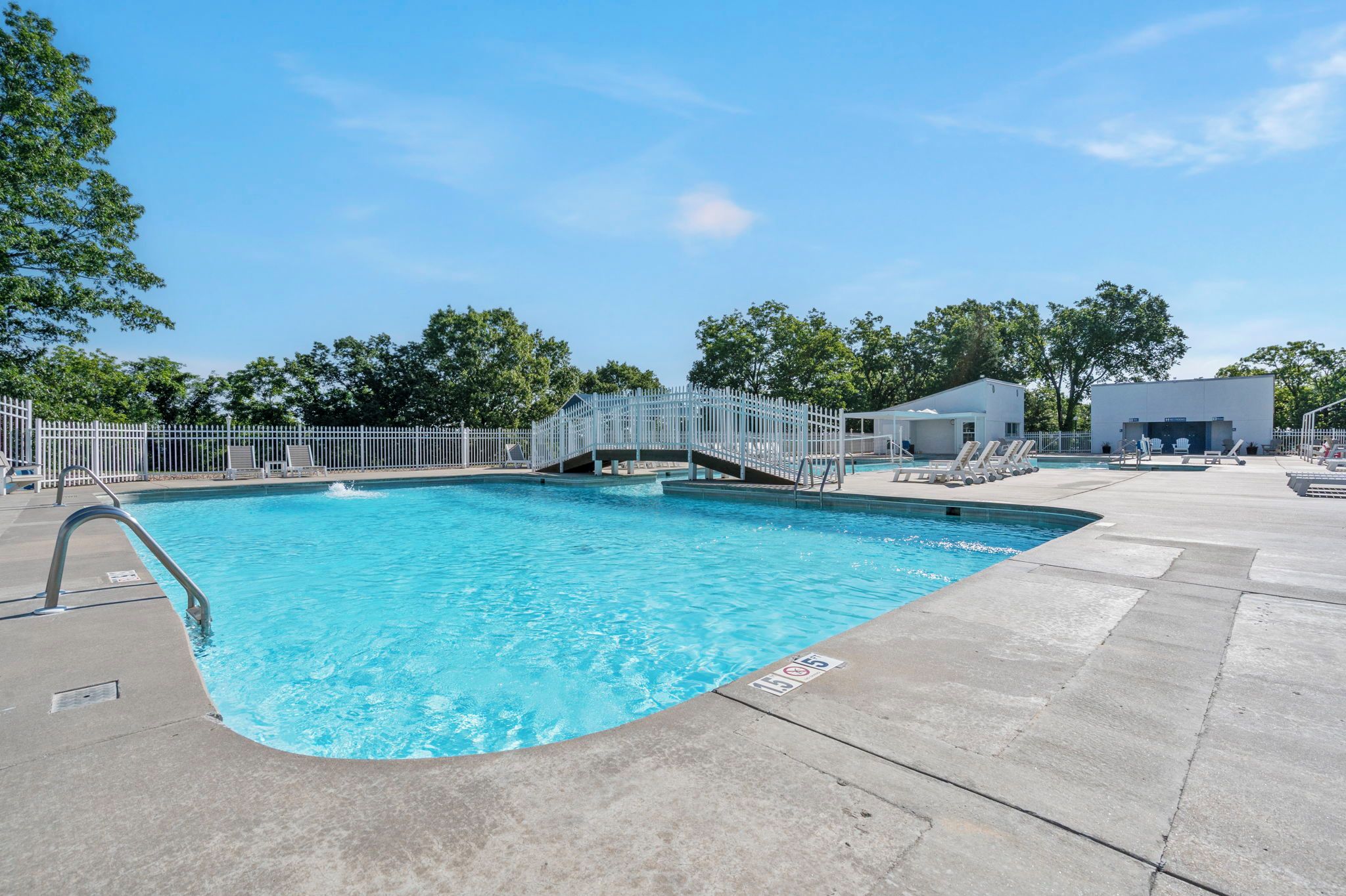 A swimming pool with a metal fence, a covered area with lounge chairs, and a building in the background.