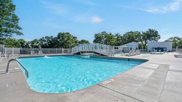 A swimming pool with a metal fence, a covered area with lounge chairs, and a building in the background.