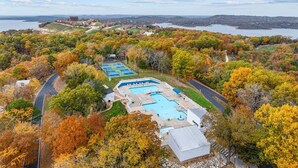 A resort with a large swimming pool, tennis courts, and a scenic view of a lake and forest.