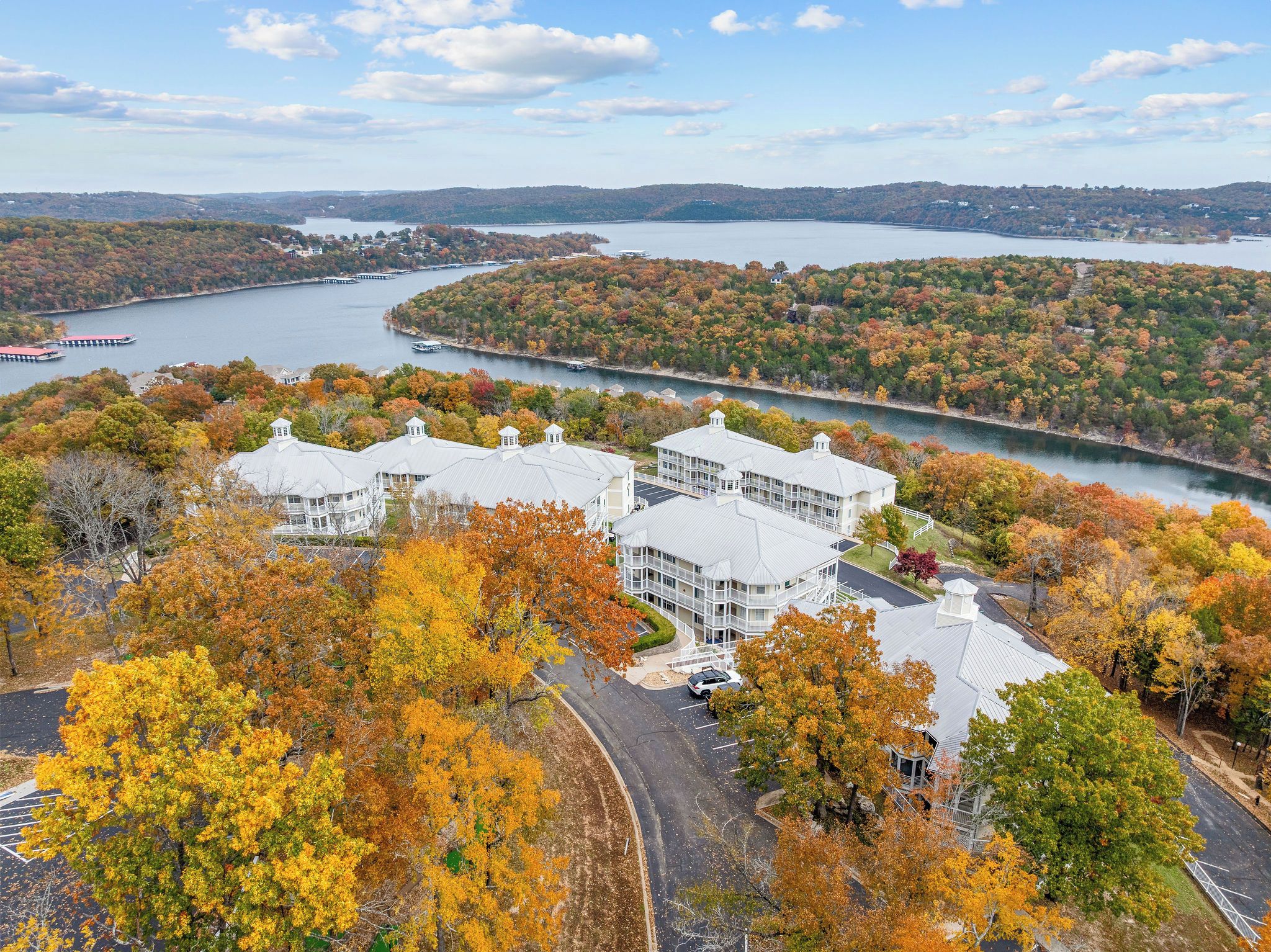 A multi-story building with a parking lot and a view of a lake and forested hills.