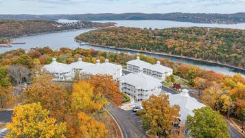A multi-story building with a parking lot and a view of a lake and forested hills.