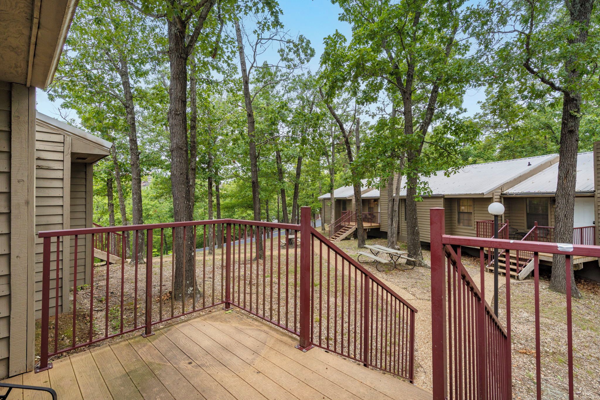 A wooden deck with a red railing leading to a covered area with picnic tables.