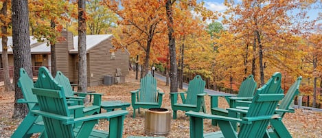 A rustic cabin with Adirondack chairs and a fire pit in a forested area.