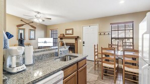 A kitchen with granite countertops, wooden cabinets, a coffee maker, and a dining area with wooden chairs.