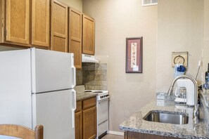 Una cocina con armarios de madera, un refrigerador blanco, una estufa, encimeras de granito y un lavamanos de acero inoxidable.