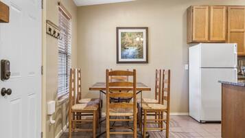 A kitchen with a dining table, chairs, a refrigerator, wooden cabinets, and a framed picture on the wall.