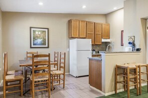 A compact kitchen with wooden cabinets, a white refrigerator, a dining table with chairs, and a small island with a sink.