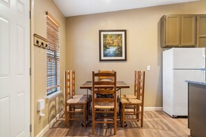 Una cocina con una mesa de comedor, sillas, un refrigerador y una ventana con persianas.