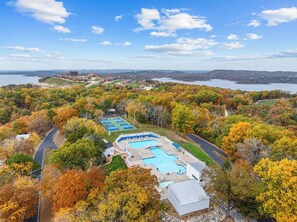 A resort with multiple swimming pools, surrounded by autumn foliage and a lake view.