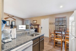 A modern kitchen with granite countertops, a built-in dishwasher, and a dining area with wooden chairs.