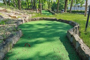A miniature golf course with a green putting surface, surrounded by stone walls and trees.