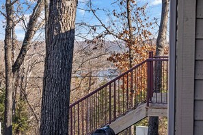 Una terraza de madera con baranda de metal que da a un bosque con follaje otoñal.