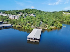 Una propiedad junto al lago con un muelle que se adentra en el agua, rodeada de abundante vegetación y edificios residenciales.