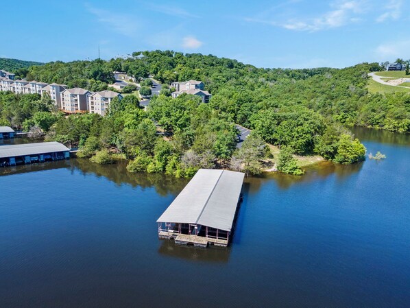 Una propiedad junto al lago con un muelle que se adentra en el agua, rodeada de abundante vegetación y edificios residenciales.
