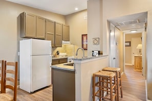 A compact kitchen with a refrigerator, sink, and wooden stools.