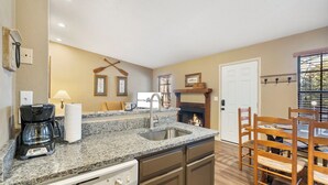 A kitchen with a granite countertop, a coffee maker, a sink, and a dining area with wooden chairs and a table.