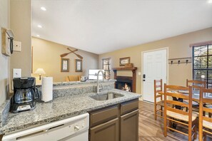 A kitchen with a granite countertop, a coffee maker, a sink, and a dining area with wooden chairs.