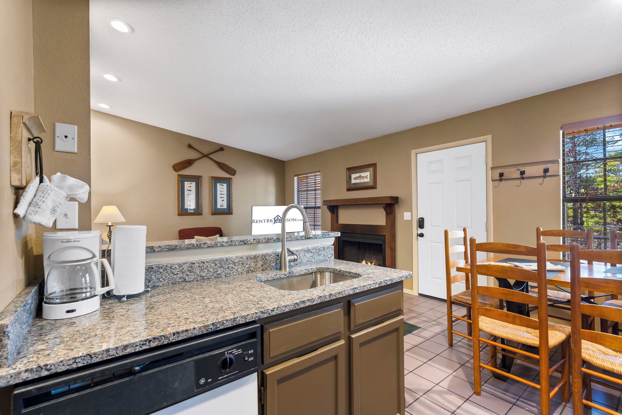 A kitchen with granite countertops, a dishwasher, a coffee maker, and a dining area with wooden chairs.