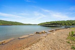 Vista de un lago con un muelle que se adentra en el agua, rodeado de terreno rocoso y exuberante vegetación.
