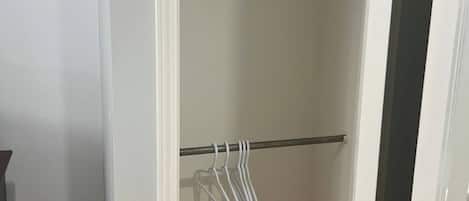A walk-in closet with two rows of white hangers on metal rods.