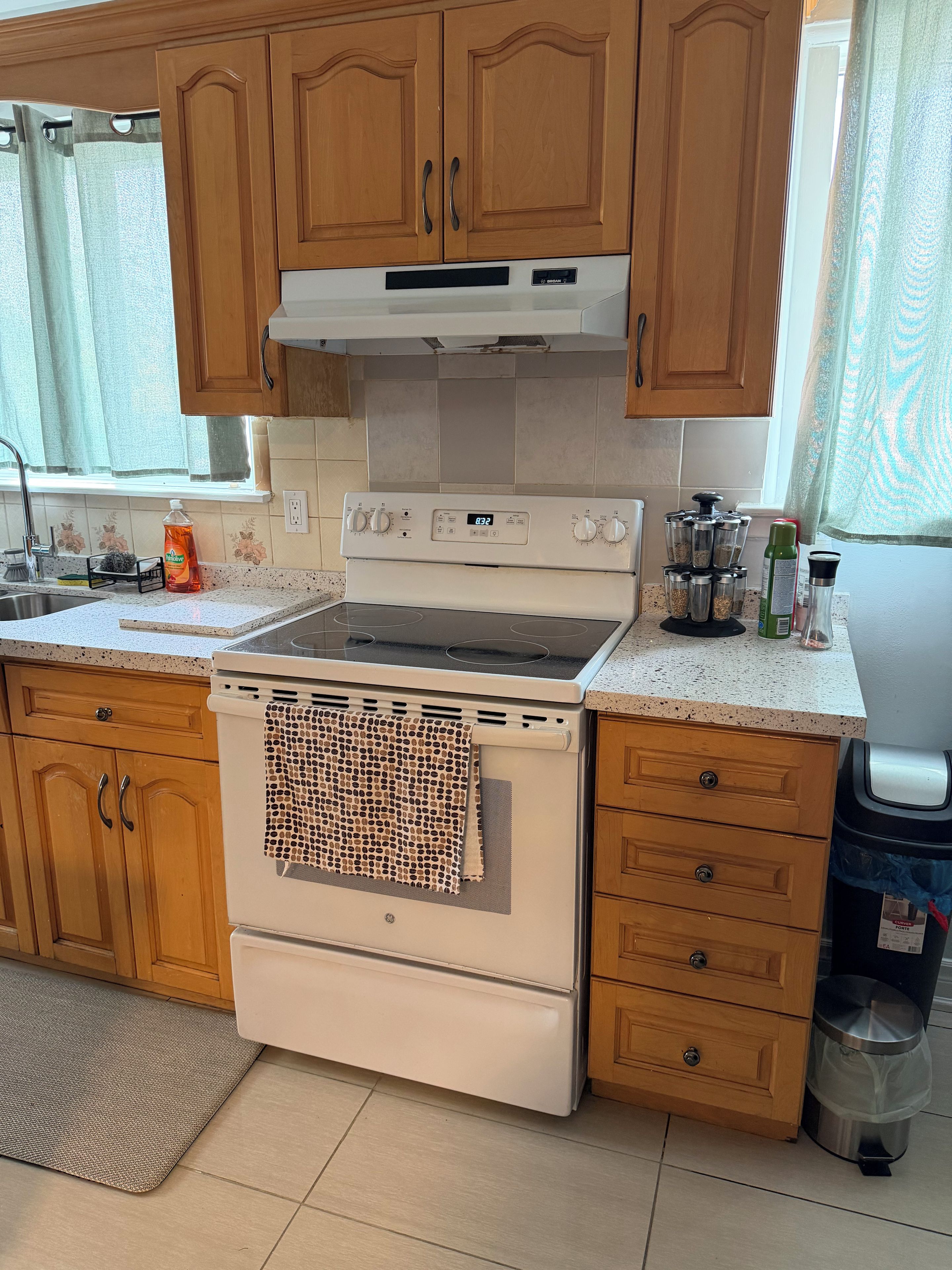 Een keuken met houten kastjes, een witte oven en een roestvrijstalen afvalbak.
