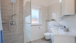 A modern bathroom with a glass shower enclosure, a toilet, a sink with a mirror, and a window.