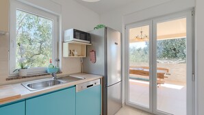 A modern kitchen with a sink, microwave, and refrigerator, a window with an orchid, and a sliding glass door to an outdoor area.