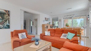 A modern living room with orange sofas, a glass coffee table, and a view of the kitchen and dining area.